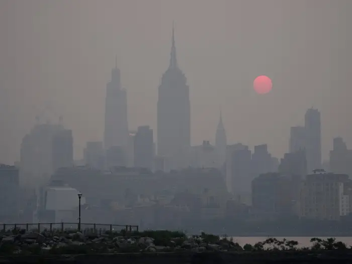 A city skyline blurred by heavy smoke haze, with a red sun above it